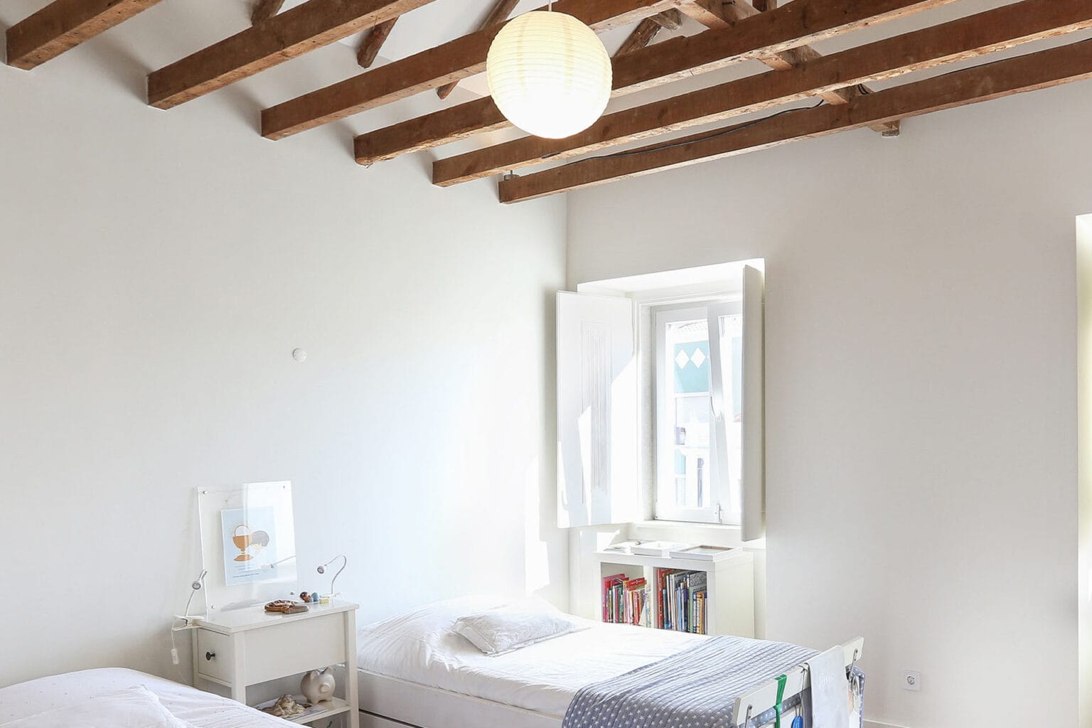 Cozy bedroom in a residential villa in Ajuda, Lisbon, with white walls, wooden ceiling beams, and na.
