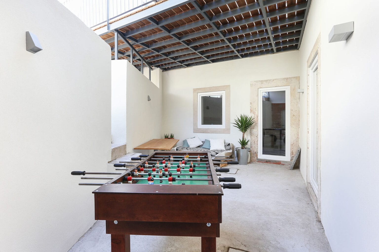 Outdoor terrace of a modern villa with foosball table, lounge chairs, and potted plants.